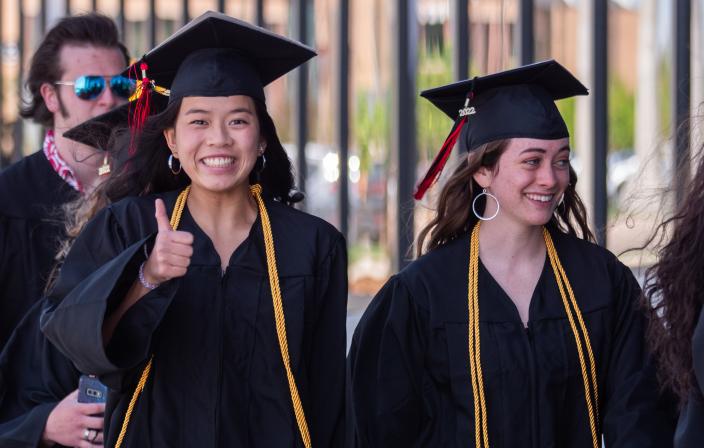 An Aims graduate making a thumbs up gesture during a commencement ceremony