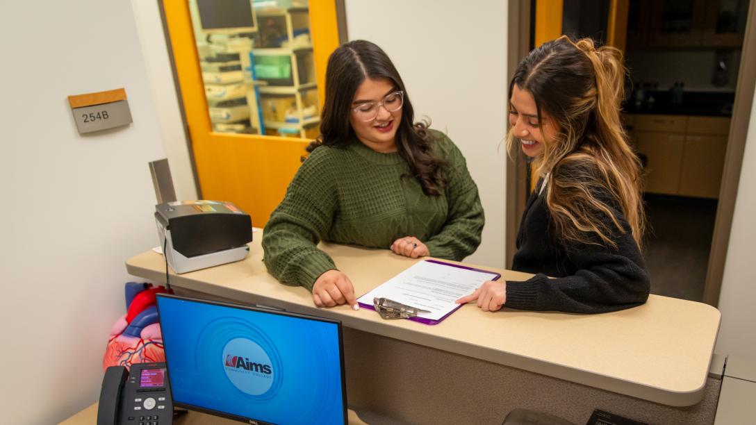 Two women looking at a clipboard on desk