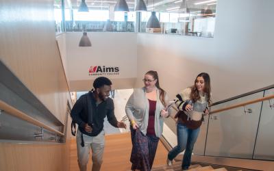 Three Aims students walking up the stairs talking as seen from at the top of the stairwell