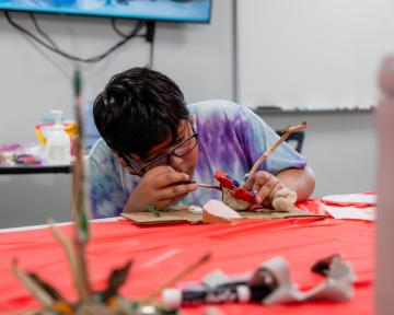 A student leans in close to paint their clay creation.