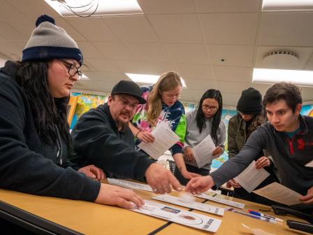 six aims students sitting at a table reviewing paperwork together